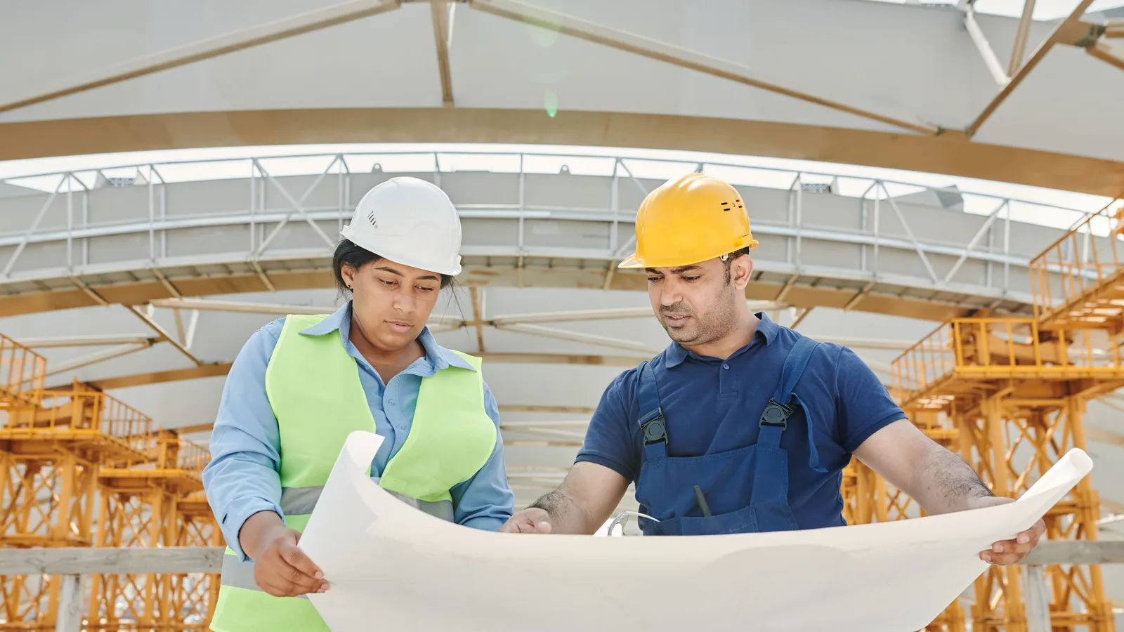 Two people in safety helmets reviewing plans