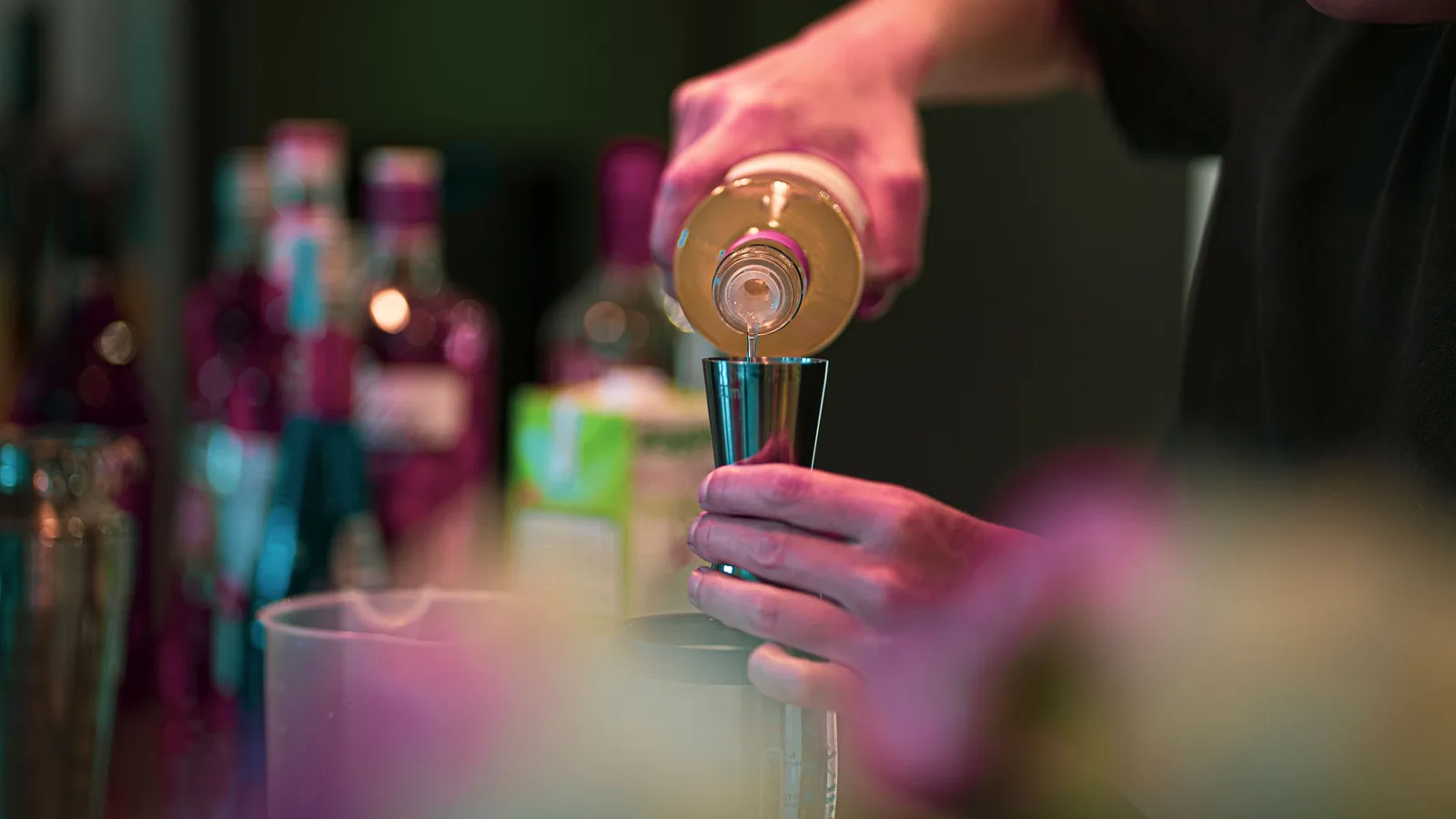Bartender pouring from a bottle into a metal jigger