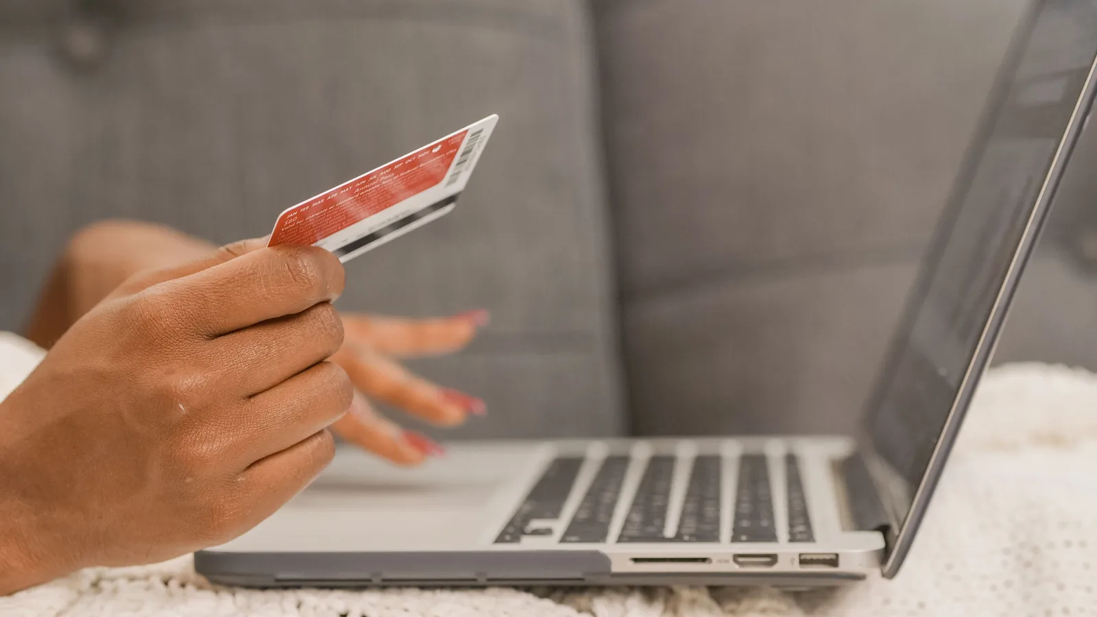 Hands holding a bank card beside an open laptop