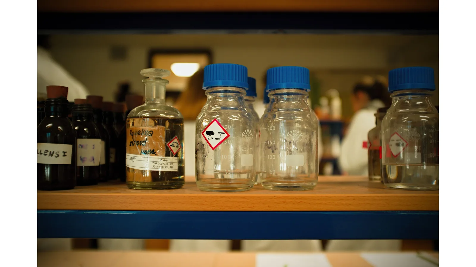 Glass chemical bottles with labels and hazard symbols on a shelf