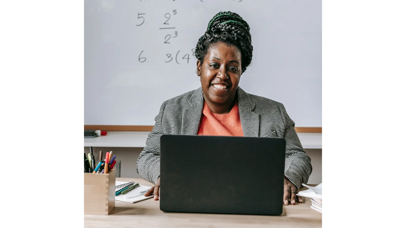 Teacher seated at a laptop in front of a classroom whiteboard