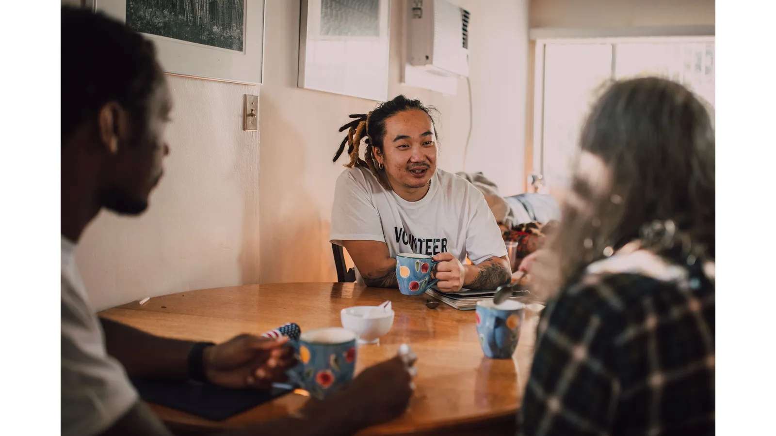 Three people talking over coffee, one wearing a volunteer shirt