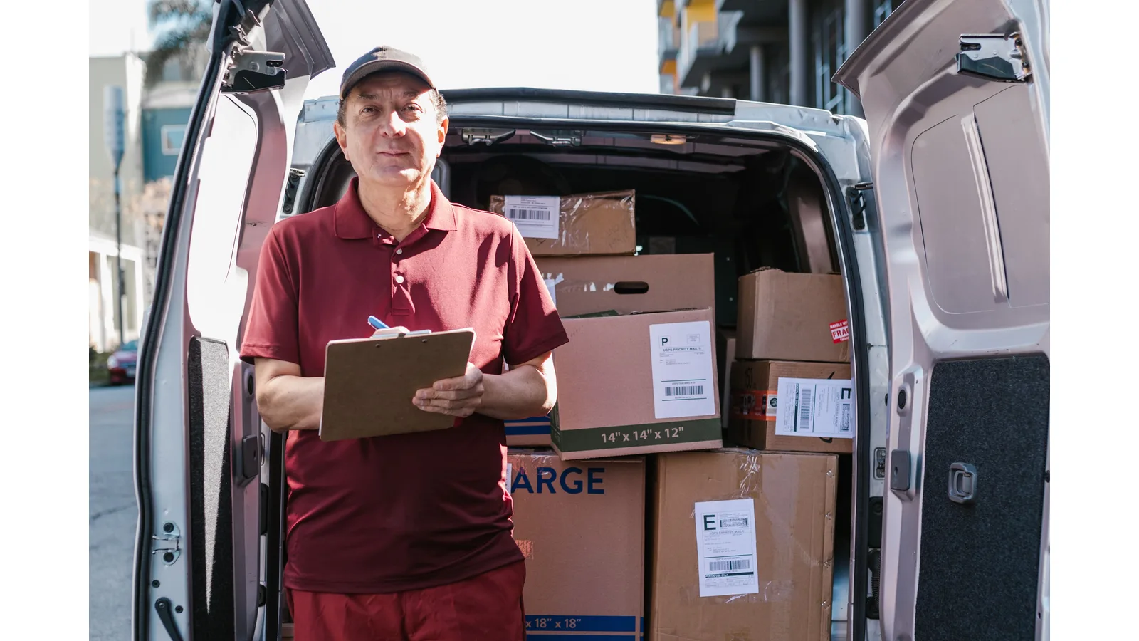 Delivery worker holding a clipboard beside a van loaded with parcels