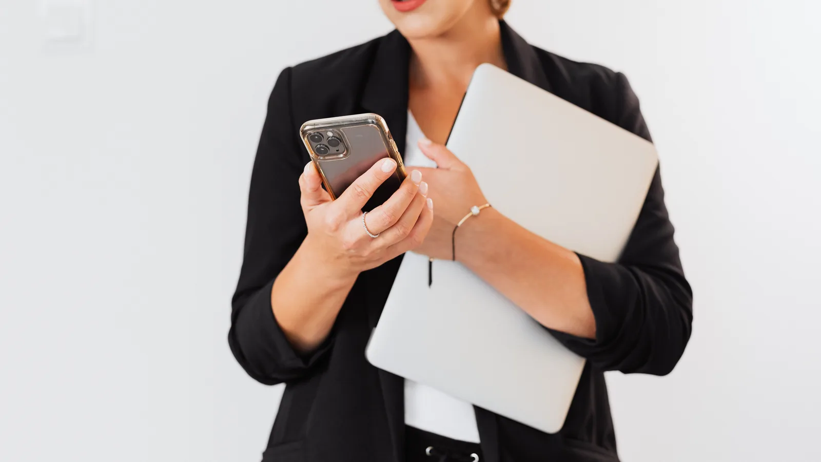 Woman using a smartphone while holding a laptop