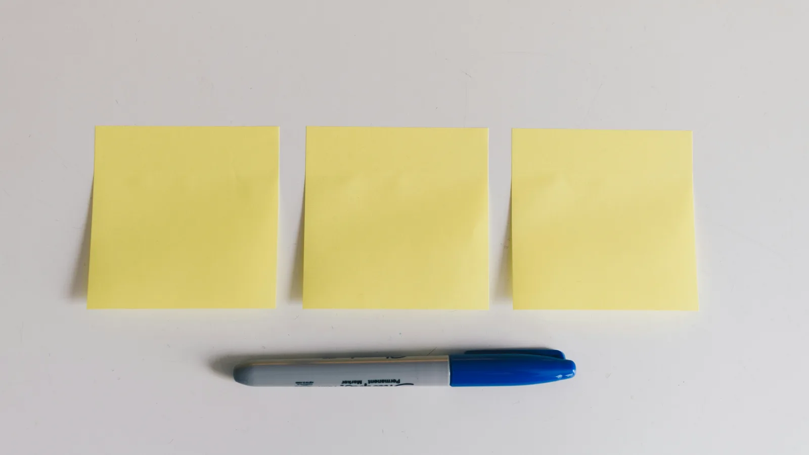 Three blank sticky notes beside a marker