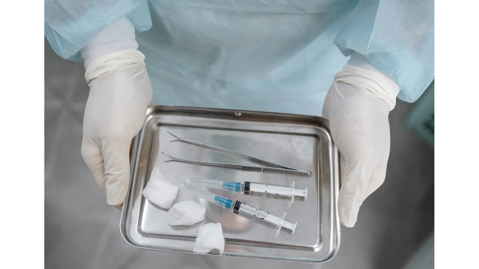 Gloved hands holding a tray of syringes and medical consumables