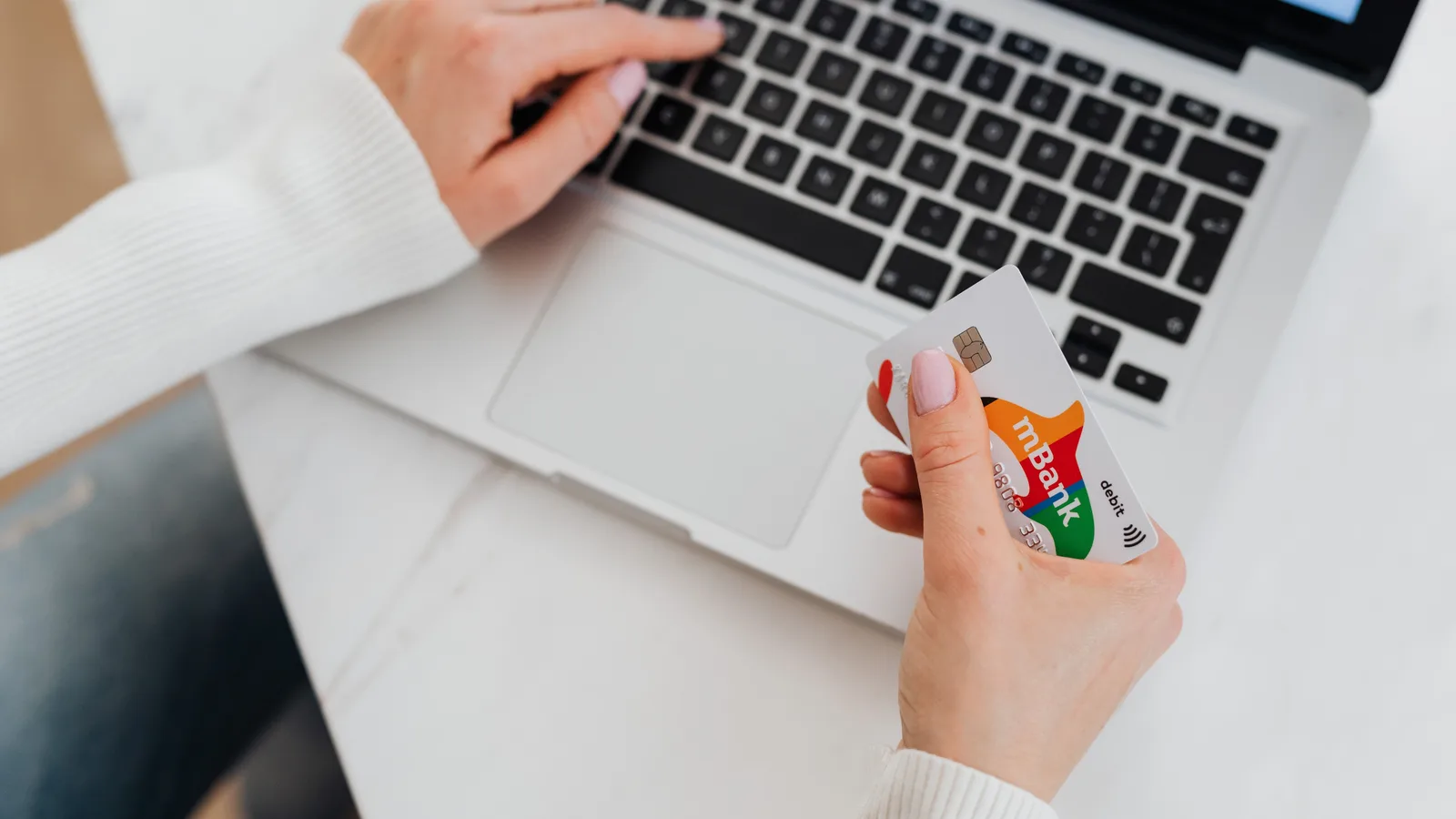 Hands holding a bank card beside an open laptop