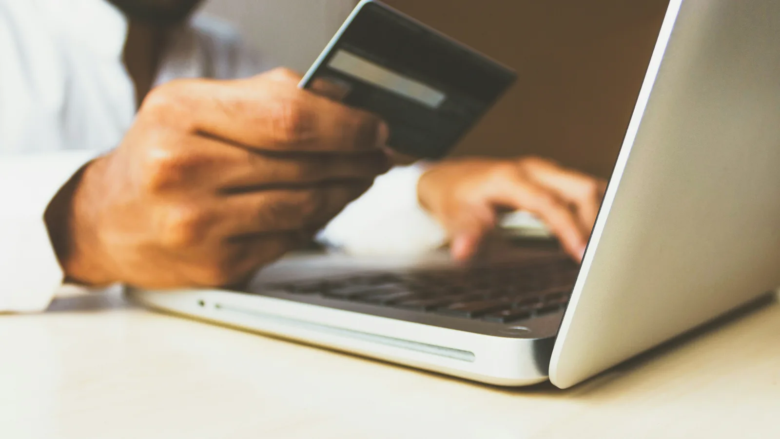 Hands holding a card beside a laptop for an online purchase