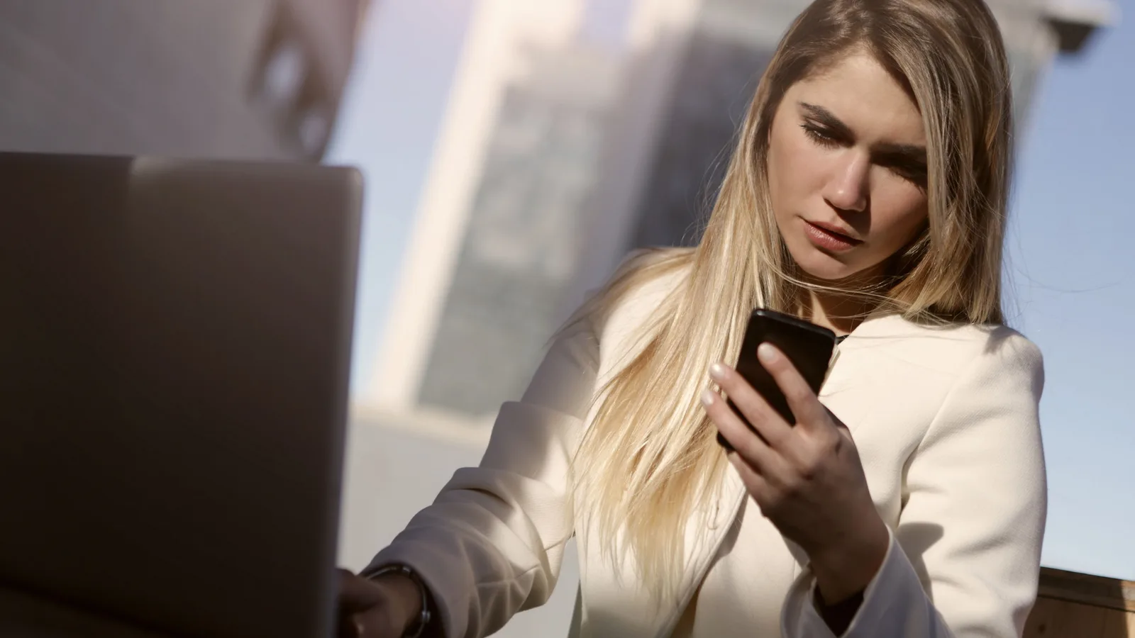 Woman reading a smartphone beside a laptop