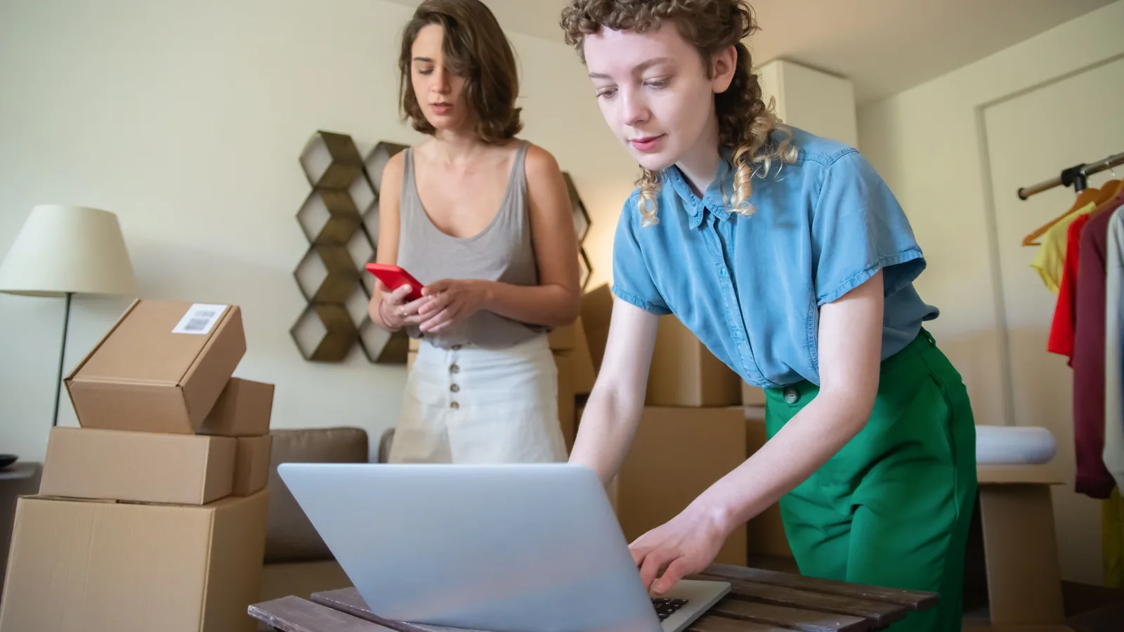Two shop workers using a laptop and phone beside parcels