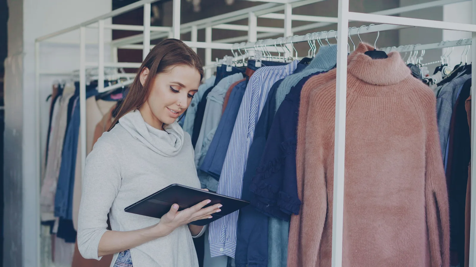 Shop worker using a tablet beside clothing rails