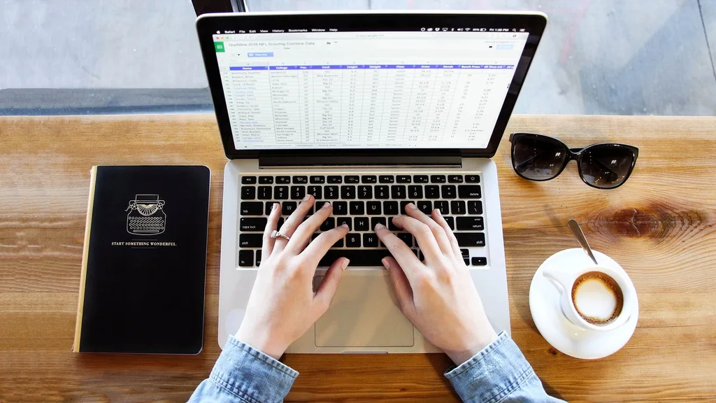 Hands typing on a laptop displaying a spreadsheet