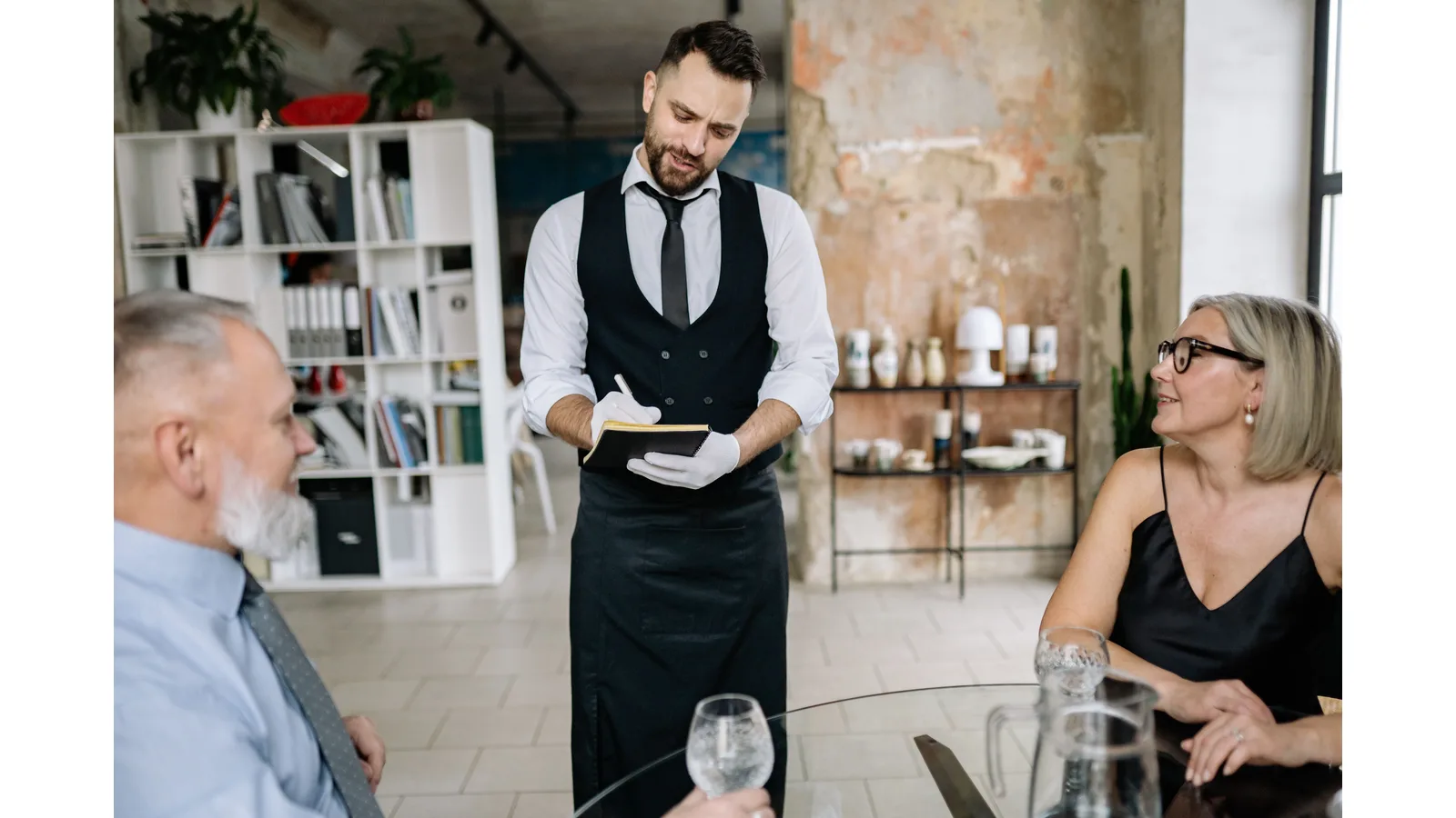 Waiter writing in a notebook beside two diners at a table