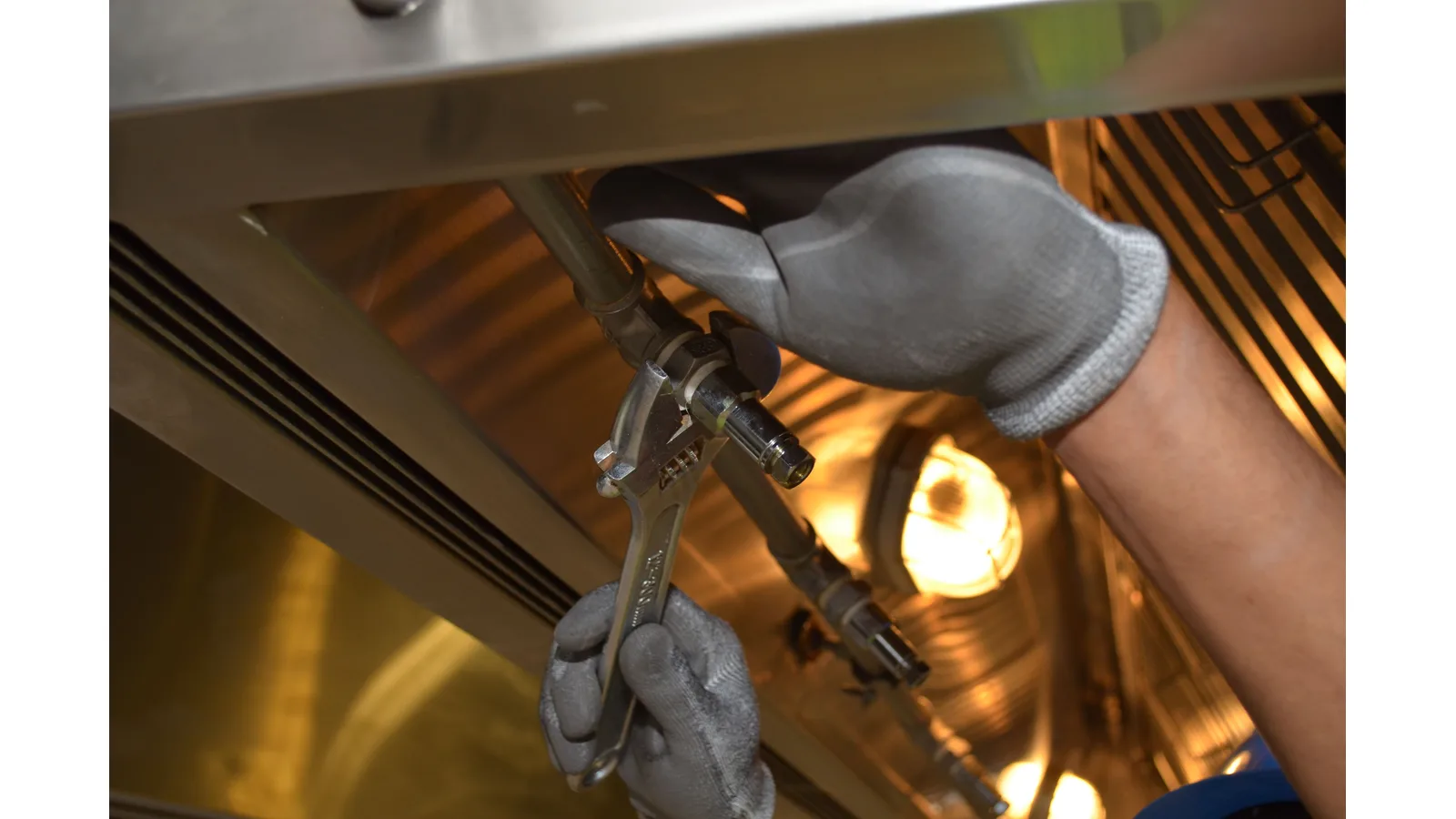 Gloved hands using tools on pipe fittings beneath a sink