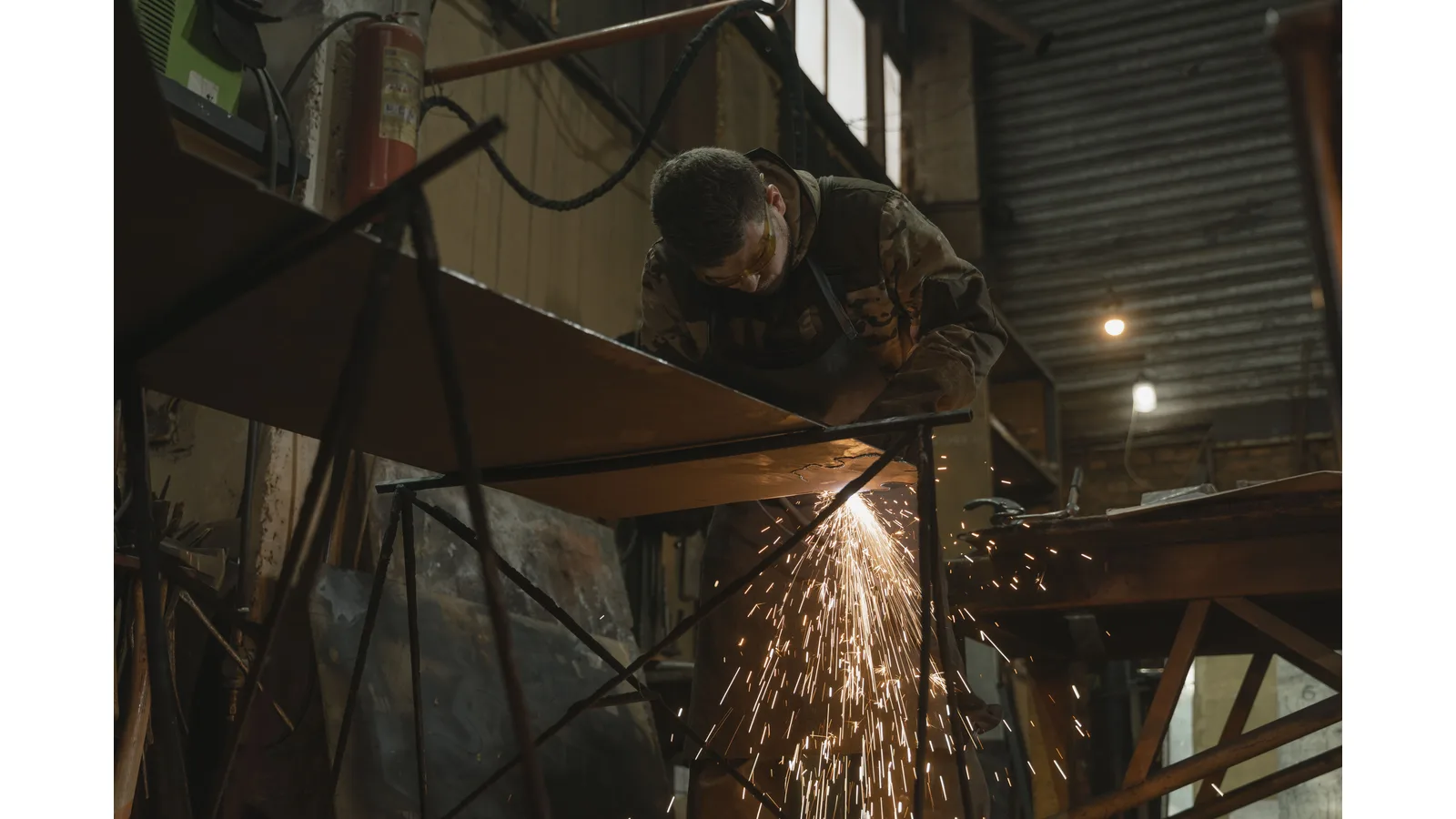 Worker using a tool on fabricated metal with sparks falling below